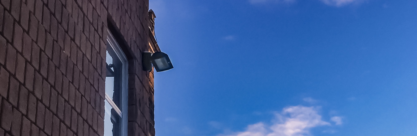 A VEK-LED wall light in mounted on the wall of a red brick building during sunset.